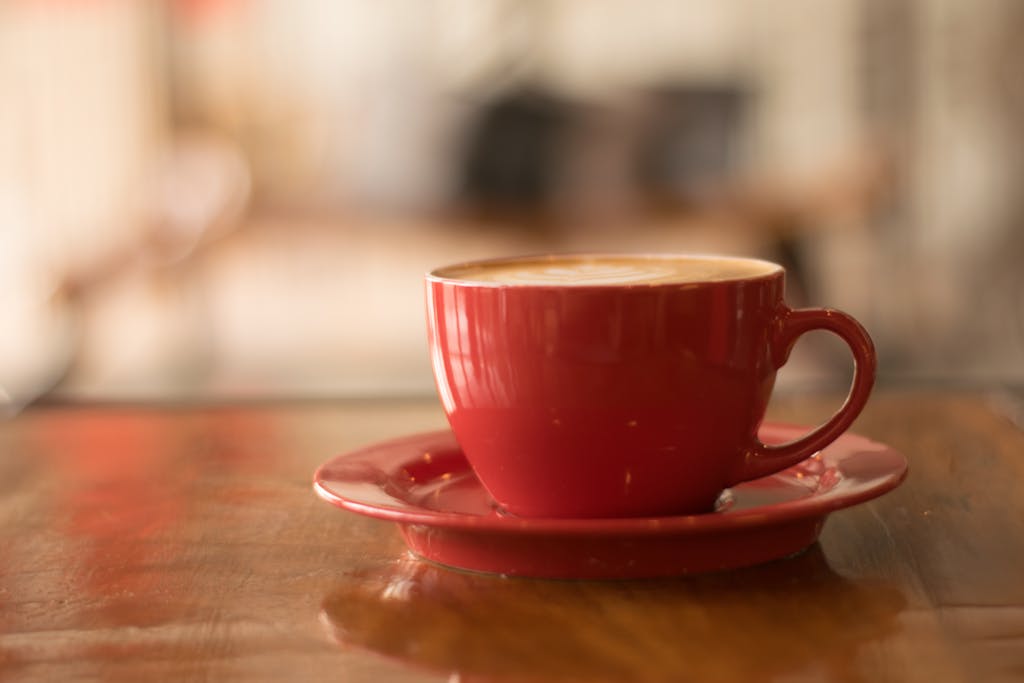 Cozy atmosphere with a cappuccino in a red cup on a wooden table, perfect for coffee lovers.