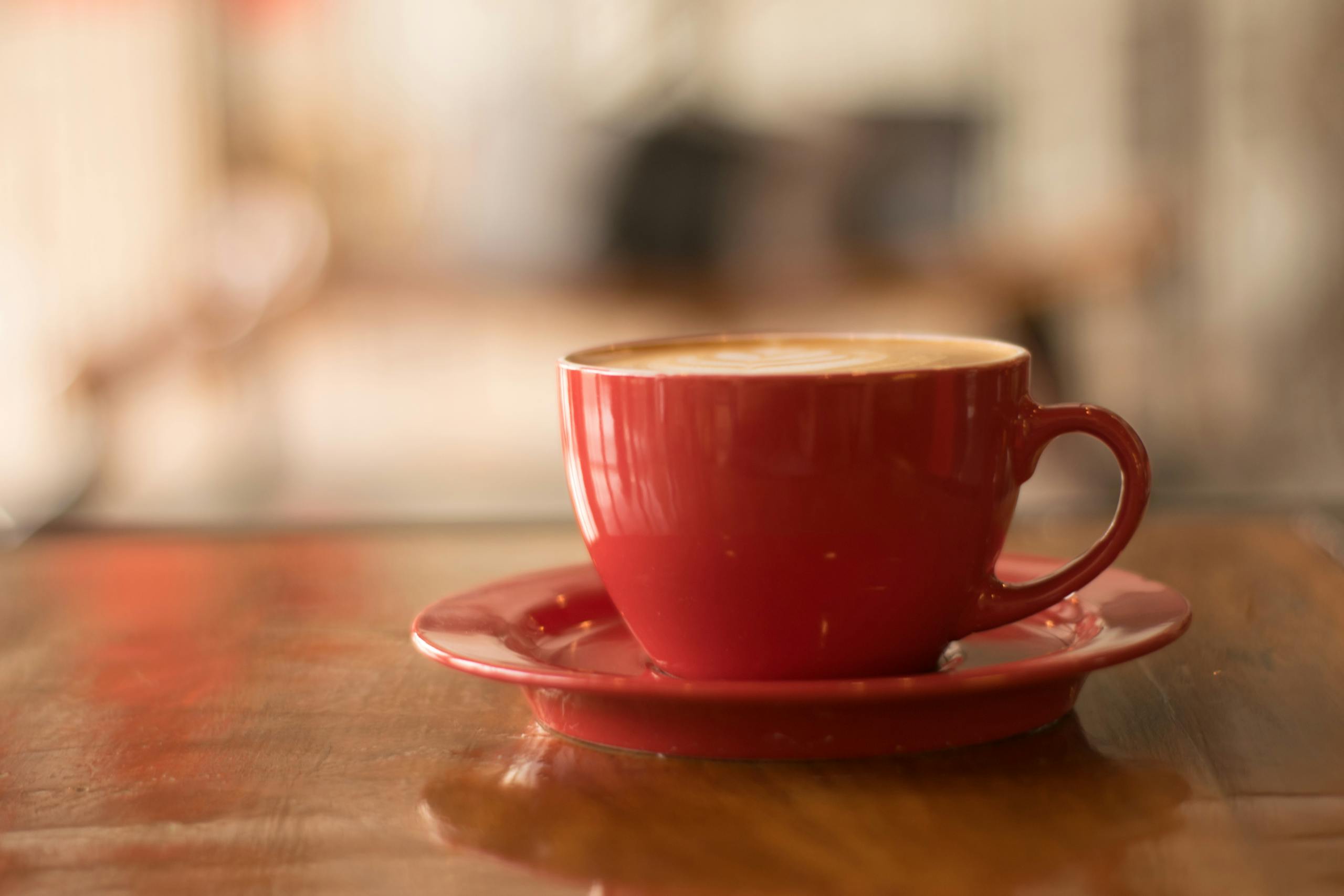 Cozy atmosphere with a cappuccino in a red cup on a wooden table, perfect for coffee lovers.