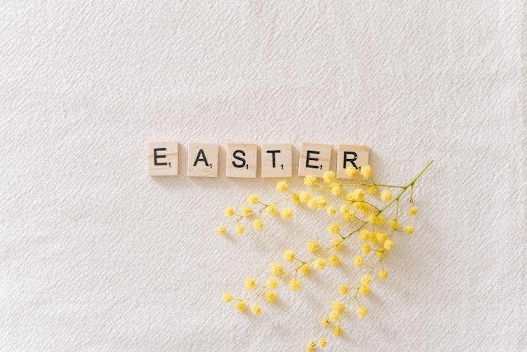 Flat lay of wooden letter tiles spelling Easter with yellow mimosa flower on textured background.